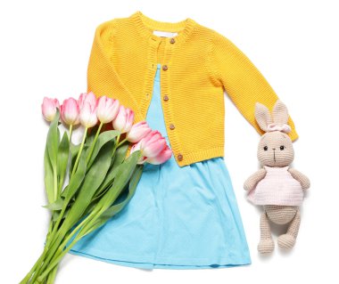 Tavşan oyuncağı ve beyaz arka planda laleleri olan küçük bir kız bahar kıyafeti.