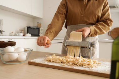 Mutfaktaki masada makineyle makarna yapan genç kadın.
