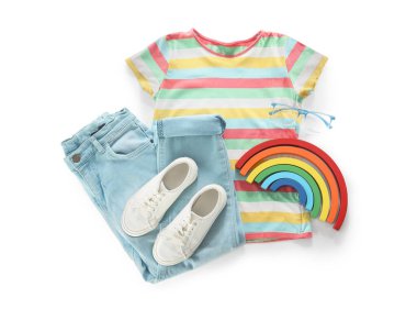 Beyaz arka planda şık çocuk kıyafetleri, ayakkabıları ve oyuncak gökkuşağı kompozisyonu
