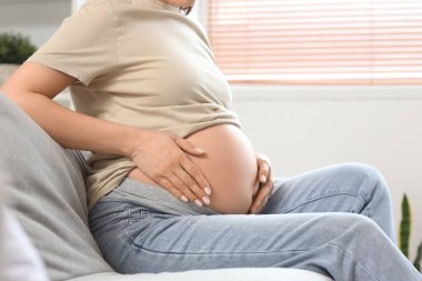 Evdeki kanepede oturan hamile bir kadın.