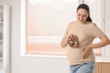 Evinin penceresinin yanında bebek poposu olan hamile bir kadın.