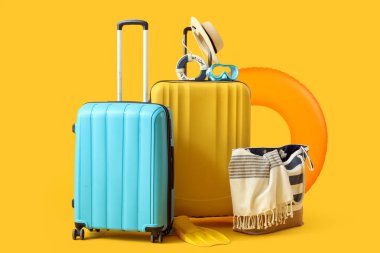 Şişme yüzüklü bavullar, yaz çantası ve sarı arka planda plaj aksesuarları. Tatil kavramı