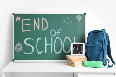 Sırt çantalı, kitaplı, saatli ve yazılı masa Işık duvarının yanındaki tahtada OKULU 'nun Sonu