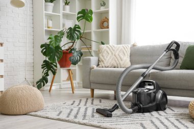 Oturma odasındaki kanepenin yanındaki halının üzerinde modern elektrikli süpürge.