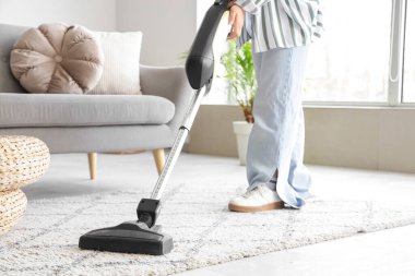 Evde süpürge temizleyen genç bir kadın var.