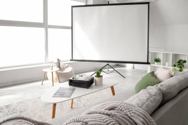 Boş projektör ekranlı, kanepeli ve masalı aydınlık oturma odasının içi.