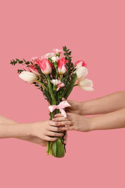 Pembe arka planda bir buket güzel çiçekli genç kadın ve tatlı kızının elleri. Anneler Günü kutlaması