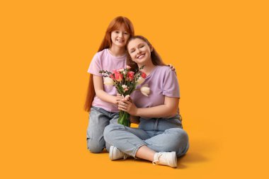 Şirin kızı elinde bir buket güzel çiçekle sarı arka planda oturan genç bir kadın. Anneler Günü kutlaması