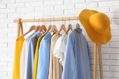 Beyaz tuğla duvarın yanında şık giysileri ve şapkası olan ahşap askı, yakın plan.