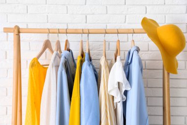 Beyaz tuğla duvarın yanında şık giysileri ve şapkası olan ahşap askı, yakın plan.