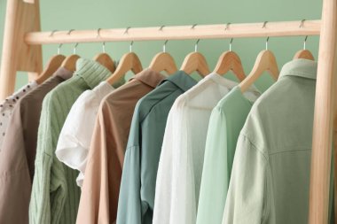 Yeşil duvarın yanında şık giysili elbise askısı, yakın plan.