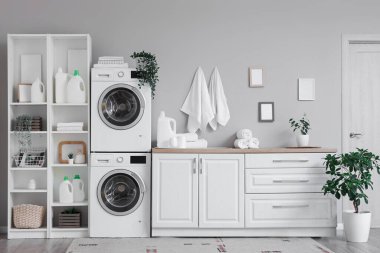 Çamaşır makineleri, raf ünitesi ve beyaz tezgahlı hafif çamaşır odasının içi.