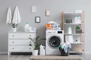 Çamaşır makinesi, kirli çamaşırlar ve raf ünitesi olan hafif çamaşır odasının içi.