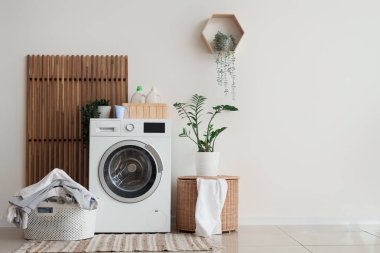 Çamaşır makinesi, çamaşır sepeti ve çiçekli şık bir banyo.