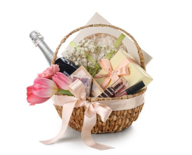 Beyaz arka planda bahar çiçekleri, şampanya ve kozmetik ürünleri olan hediye sepeti.