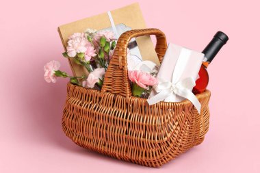 Pembe arka planda bahar çiçekleri, şarap, şeker ve kozmetik ürünleri olan hediye sepeti.