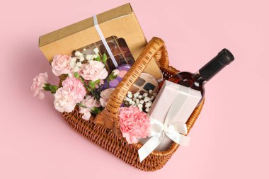 Pembe arka planda bahar çiçekleri, şarap, şeker ve kozmetik ürünleri olan hediye sepeti.