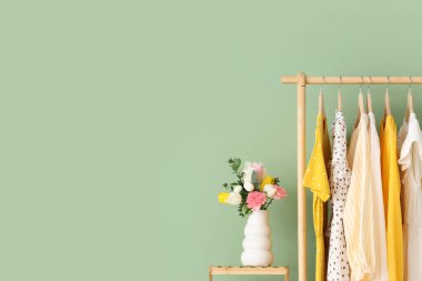 Renk duvarına karşı şık kadın kıyafetleri ve çiçeklerle dizilin.