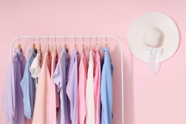 Pembe duvarda şık kadın kıyafetleri ve hasır şapkası asılı.