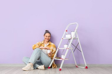 Leylak duvarının yanında boya kutuları ve merdiveni olan genç bir kadın.