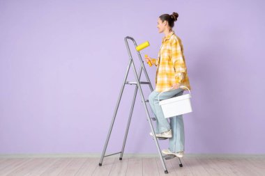 Leylak duvarının yanındaki merdivende boya ve kova taşıyan genç bir kadın.
