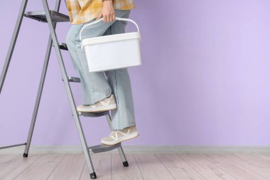 Leylak duvarının yanındaki merdivende kovası olan genç bir kadın.