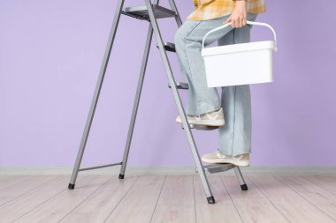 Leylak duvarının yanındaki merdivende kovası olan genç bir kadın.