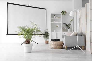 Oturma odasının içinde kanepe, puf ve projektör var.