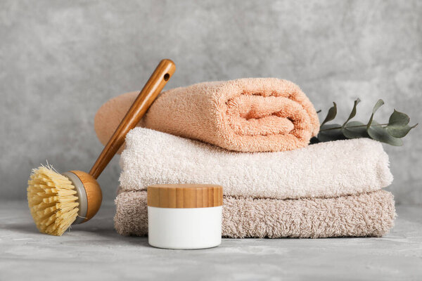 Stack of clean towels, massage brush and cosmetic product on grunge background
