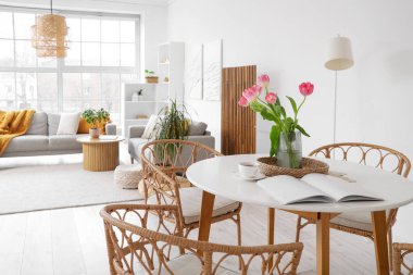 Modern stüdyo dairesindeki yemek masasında lale, bardak ve dergi olan vazo.