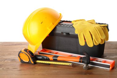 Beyaz arka plana karşı ahşap masadaki sert şapka, alet çantası ve inşaat araçları