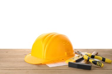 Sert şapka, ev planı ve inşaat aletleri beyaz arka plana karşı ahşap masa üzerinde