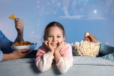 Evde film izlerken ailesiyle birlikte mutlu küçük bir kız.