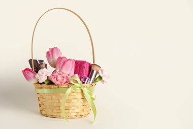 Güzel bahar çiçekleri, hediye kutuları ve renk arkaplanlı makyaj fırçalarıyla dolu bir sepet.