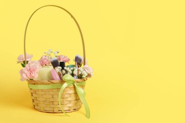 Güzel çiçekli sepet, kozmetik ürünler ve sarı arkaplanda makyaj fırçaları.