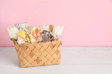 Hediye kutuları, çiçekler, parfüm şişesi ve hafif ahşap masada makyaj fırçaları olan bir sepet.