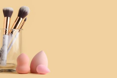 Makyaj fırçalı cam ve sarı arka planda pembe süngerler.