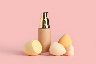 Pembe arka planda makyaj süngeri ve bir şişe fondöten.