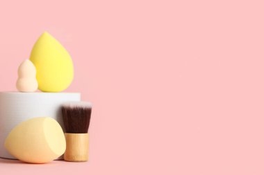 Makyaj süngerli dekoratif podyum ve pembe arka planda fırça