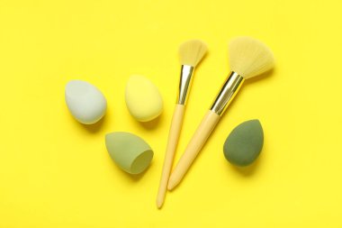 Sarı arka planda makyaj süngerleri ve fırçalar