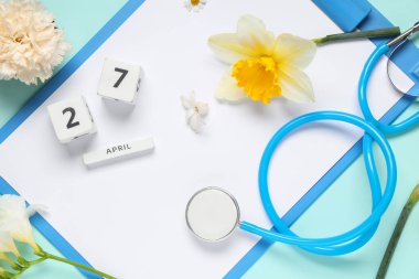 Pano, steteskop, 27 Nisan tarihli takvim ve renk arkaplan üzerinde güzel bahar çiçekleri olan kompozisyon, yakın plan
