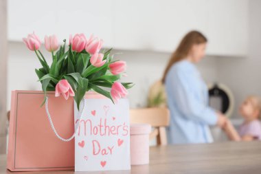 Anneler Günü için içinde lale ve kartpostal olan hediye paketi mutfakta kızı olan genç bir bayana karşı, yakın plan.