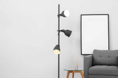 Odada ışık duvarının yanında parlayan lambasıyla gri koltuk.