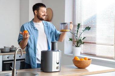 Genç adam taze portakal suyu ve modern meyve sıkacağı ile mutfakta.