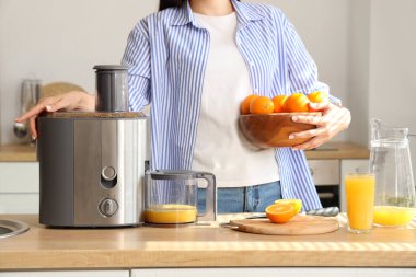 Mutfakta portakal suyu ve meyve sıkacağı olan genç bir kadın var.