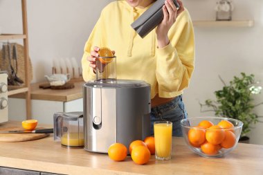 Genç bir kadın mutfakta portakal suyu yapıyor.