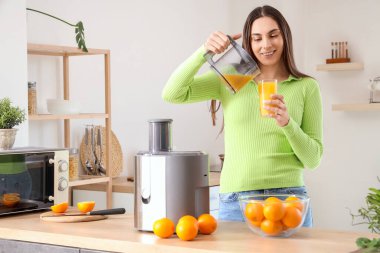 Modern meyve sıkacağıyla mutfağa portakal suyu döken genç bir kadın.