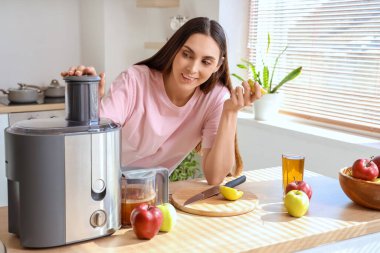 Mutfaktaki masada elma suyu ve meyve sıkacağı olan genç bir kadın.