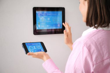 Cep telefonlu genç bir kadın akıllı ev güvenlik sistemi kontrol panelini kullanıyor.