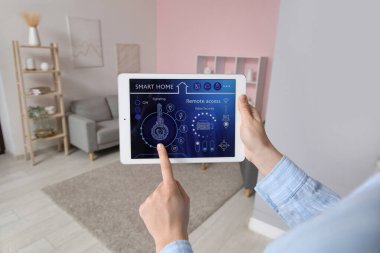 Odada akıllı ev güvenlik kontrol paneli olan tablet kullanan kadın eller